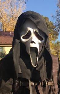 person in a neighborhood wearing a Ghostface mask and cloak