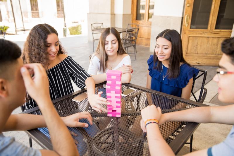 Beautiful teenage girl playing board games with friends at coffee shop