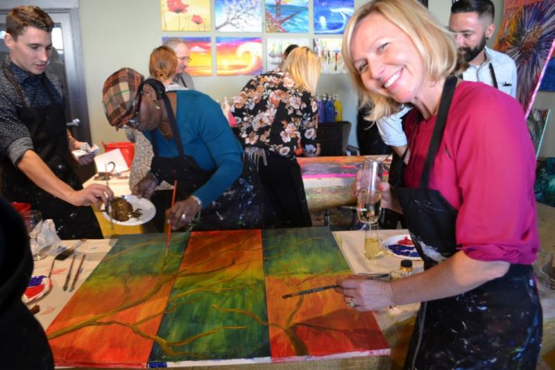 Men ans women drinking wine and painting on canvas.