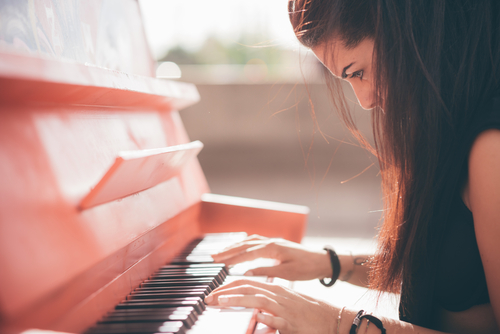 Close up of a young beautiful reddish brown hair caucasian girl playing piano - creative_ performance_ music concept - she is dressed with a black shirt and plays a red piano